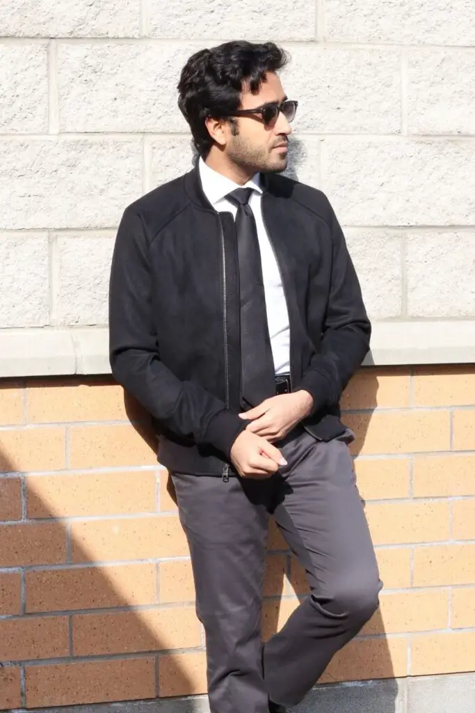 black suede jacket with white dress and grey chinos, black tie and ray ban glasses